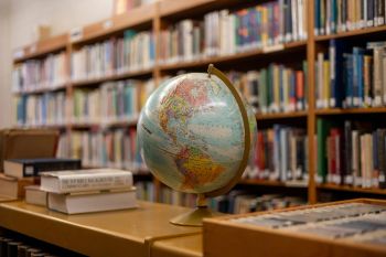 A globe on a library shelf in front of rows of books