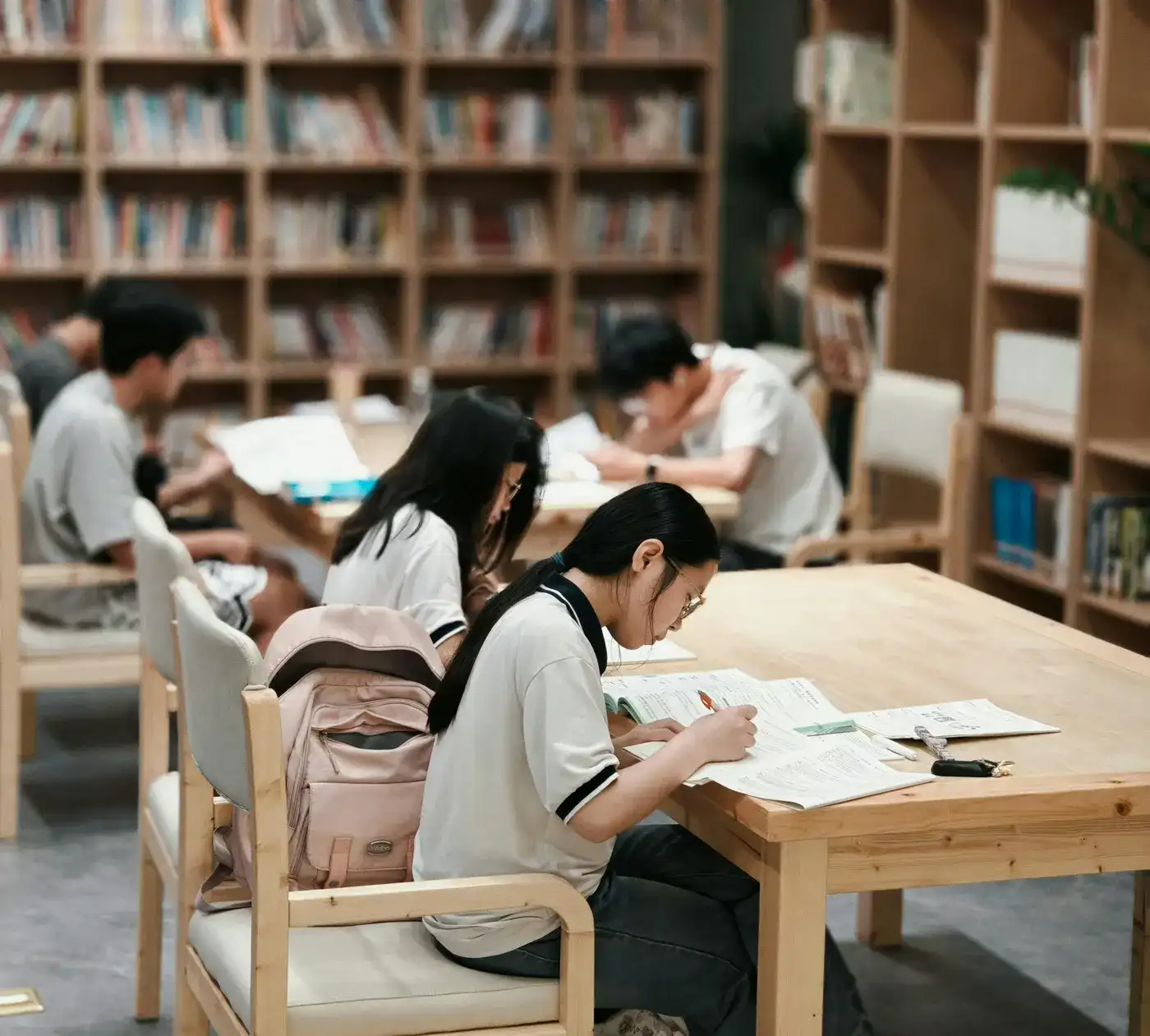 図書館の机で、制服姿で問題集に書き込みをして勉強する高校生たち